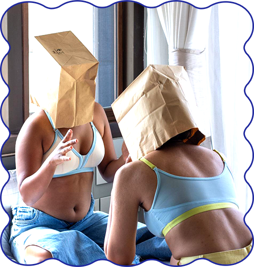 Two people sitting on a couch with paper bags over their heads, wearing underwear and shorts.