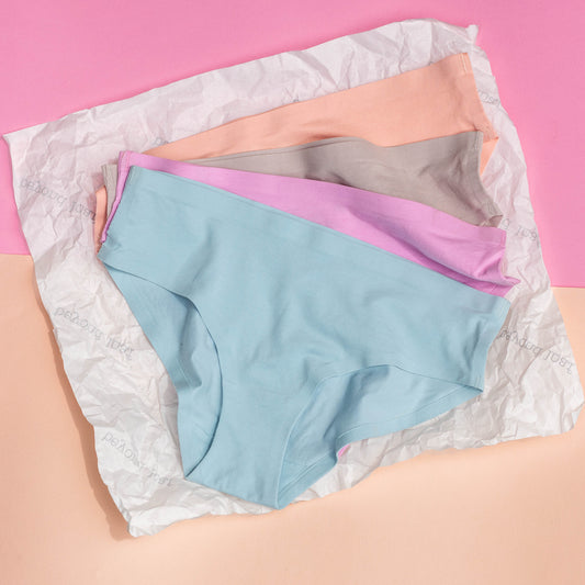 Four pairs of underwear in  peach, blue, pink, and gray on a textured white surface with a pink background.