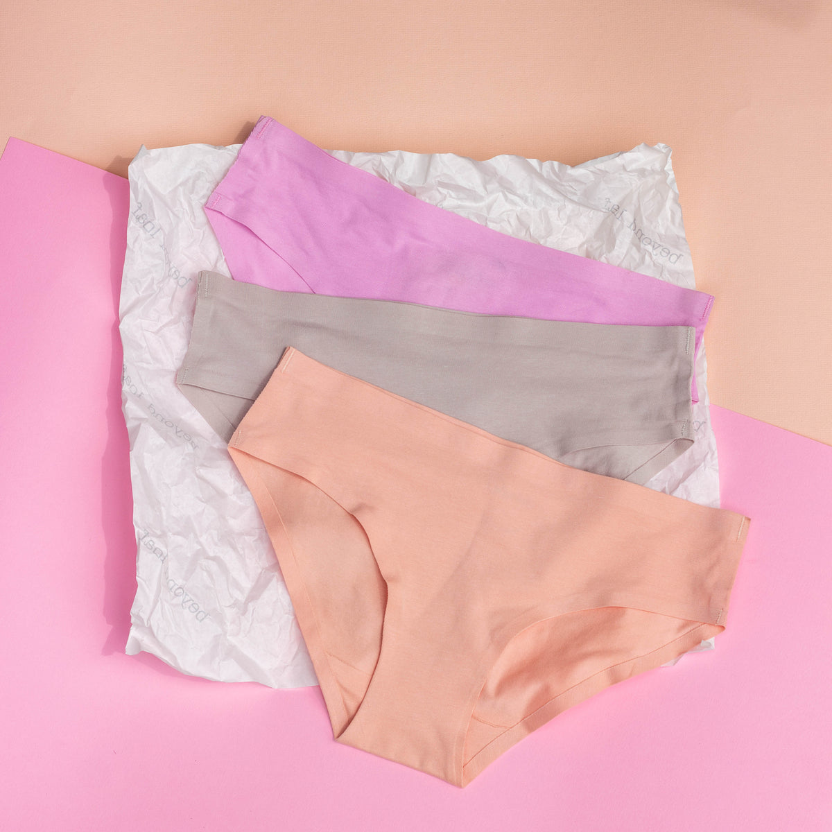 Three pairs of underwear in pink, gray, and peach on a pink background