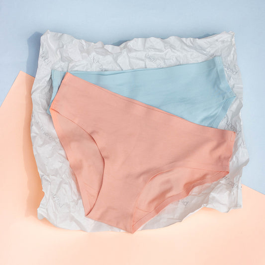 pair of pastel-colored underwear in peach and blue, on a textured surface with a light blue background