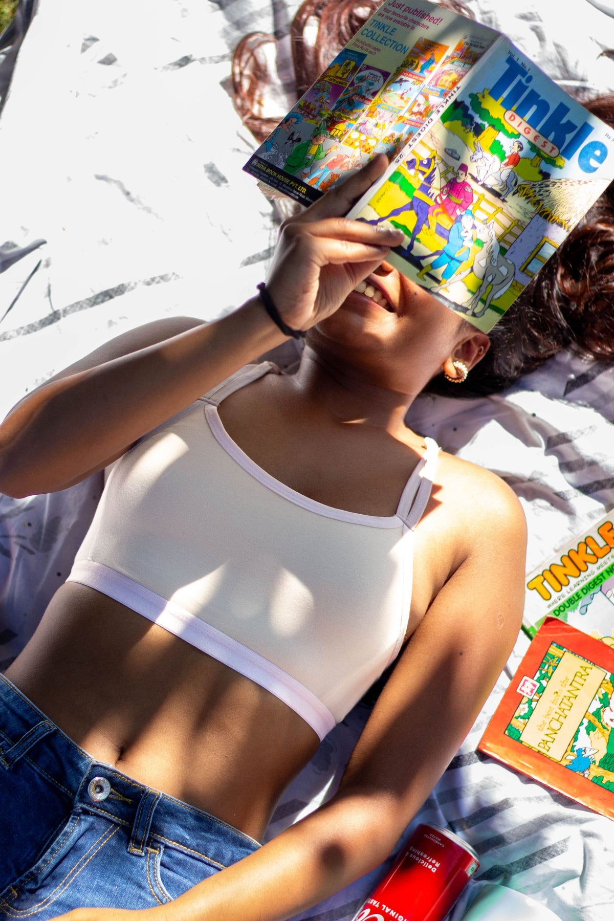 Person holding a magazine, lying down in a qiwion jumpstart bra in a light cream colour, with a pair of shorts.