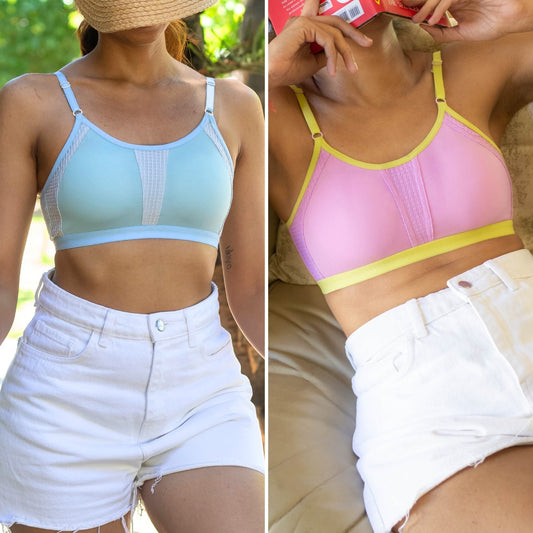 Two women wearing sports bras and shorts, one in a light blue bra and white shorts, the other in a pink bra with yellow straps and white shorts.