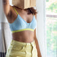 Person wearing a light blue bra and yellow pants with a paper bag over their head indoors.