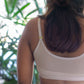 Person wearing a beige sports bra with blurred green foliage in the background