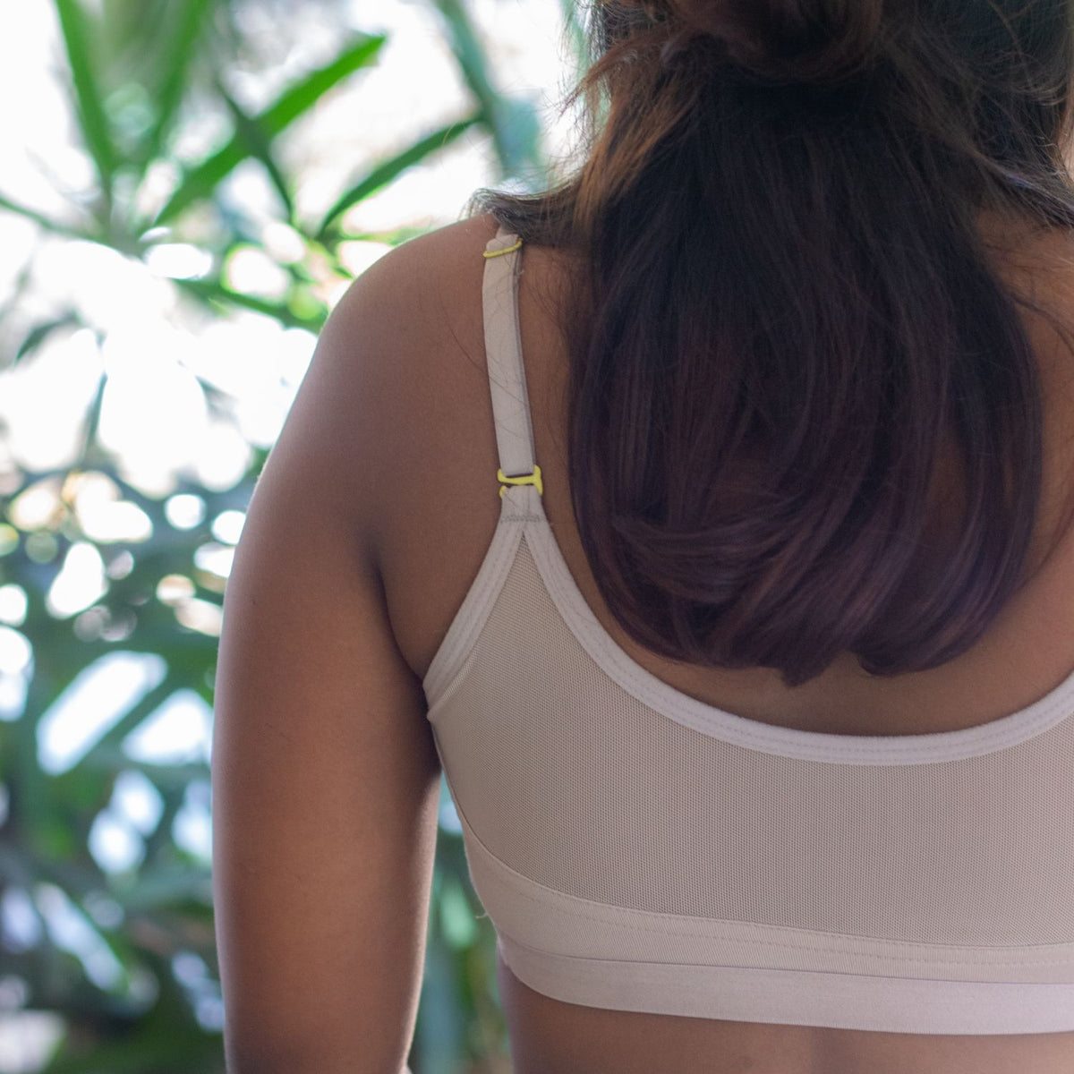 Person wearing a beige sports bra with blurred green foliage in the background