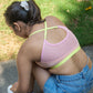 Person wearing Qiwion Mood bra with mesh back. The straps are in a neon, and criss crossed. While the bra is a light pink shade. 