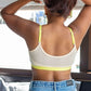 Qiwion Mood Youth Bra in a cream and neon colour. Padded, non-wired bra with adjustable straps. The woman shoes the adjustable straps and the mesh back