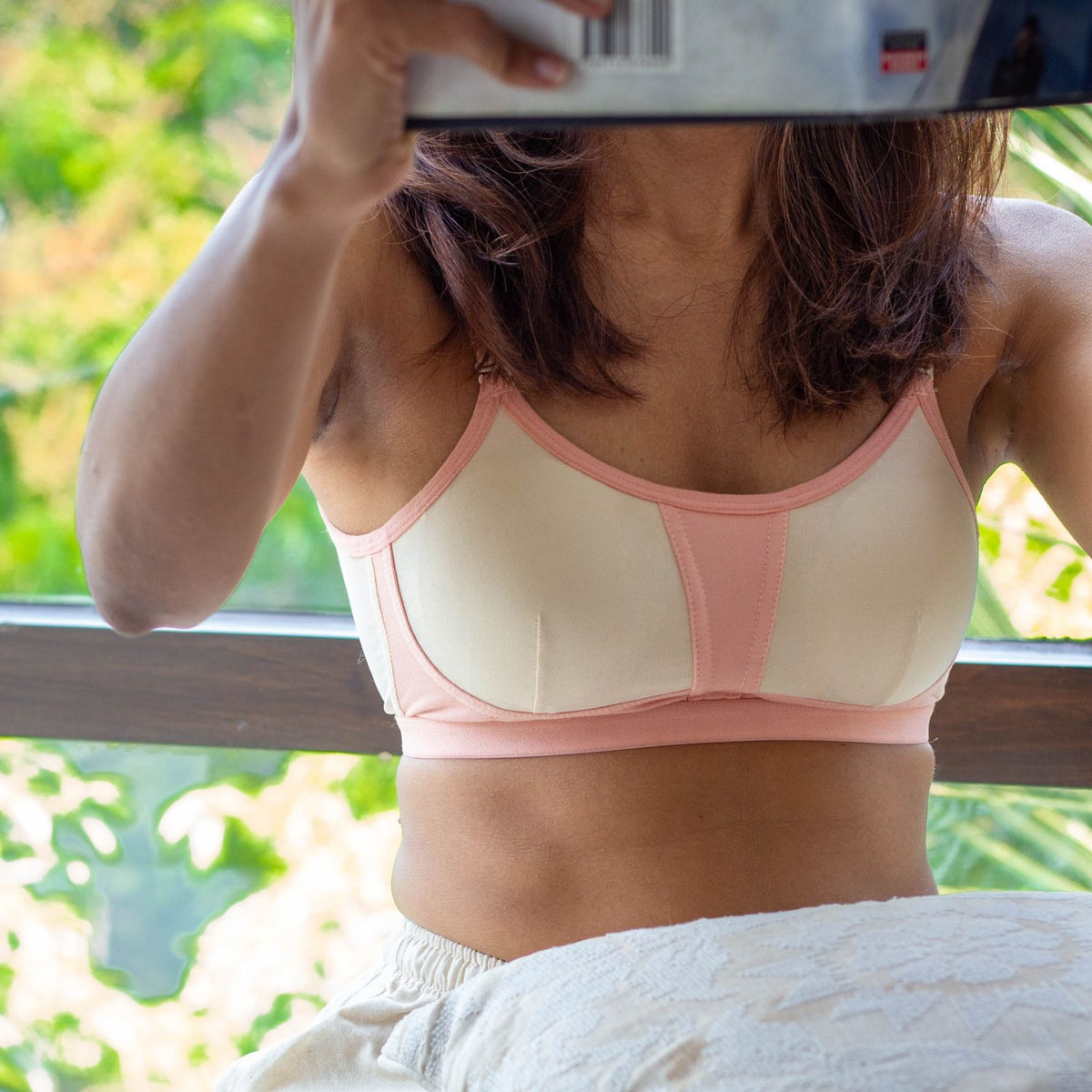 Person wearing a pink and cream qiwion bra with a blurred outdoor background