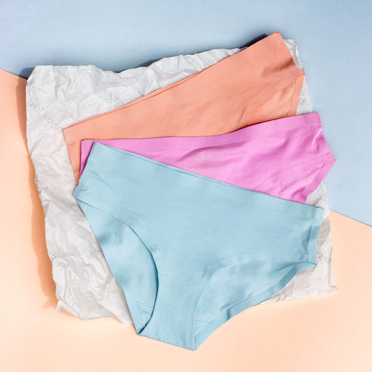 Three pairs of blue, pink, peach underwear on a textured surface with a light blue background