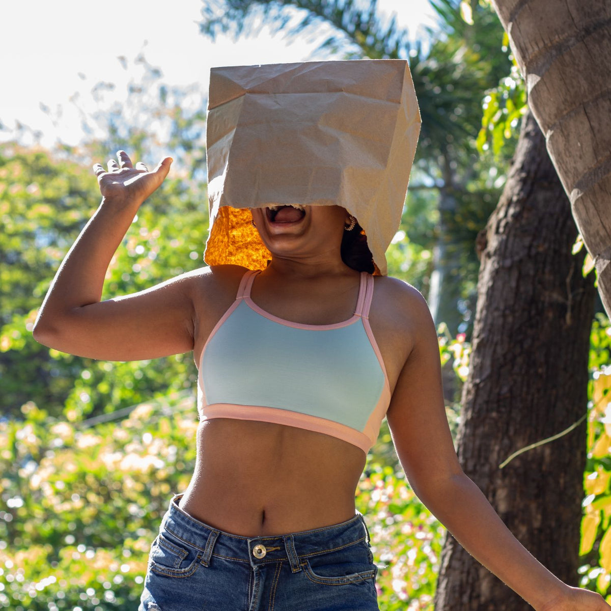 Person wearing a light blue beginner bra and jeans with a paper bag over their head outdoors.